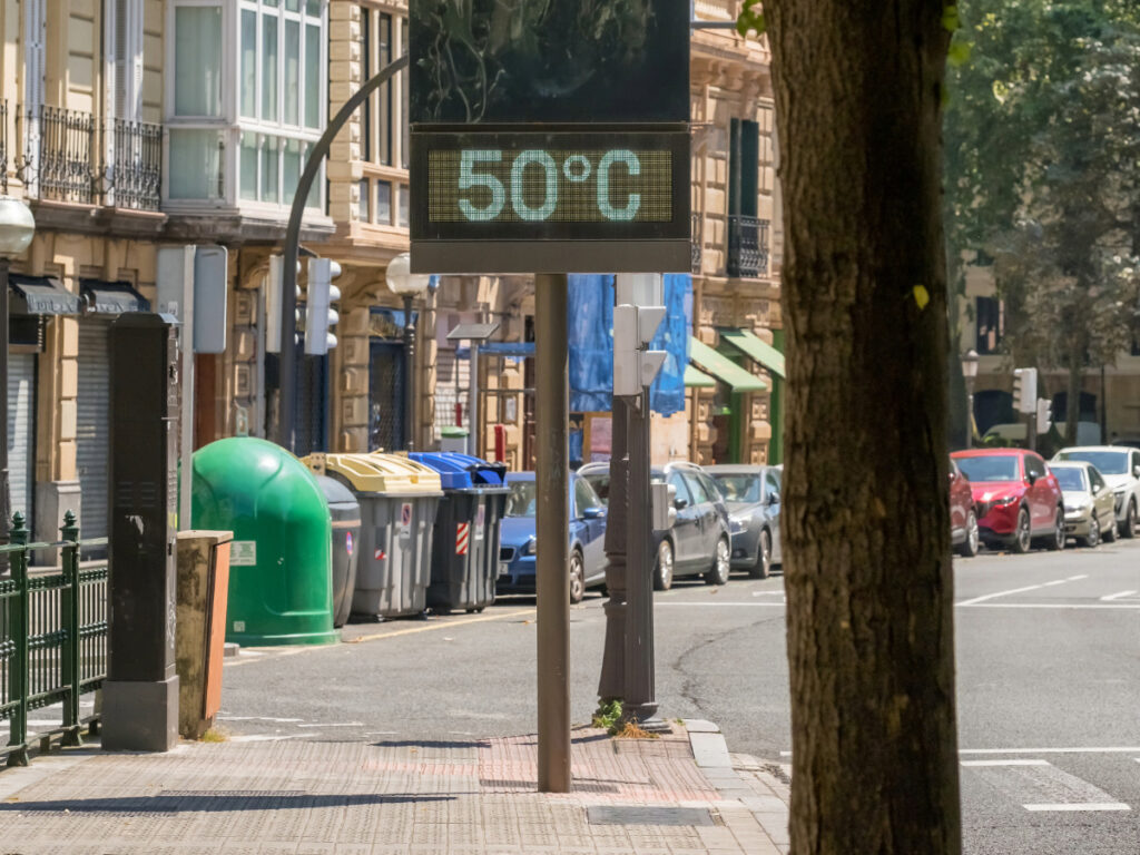 Blick in die Straßenschneise einer Stadt. Im Vordergrund zeigt ein Thermometer 50 Grad Celsius.