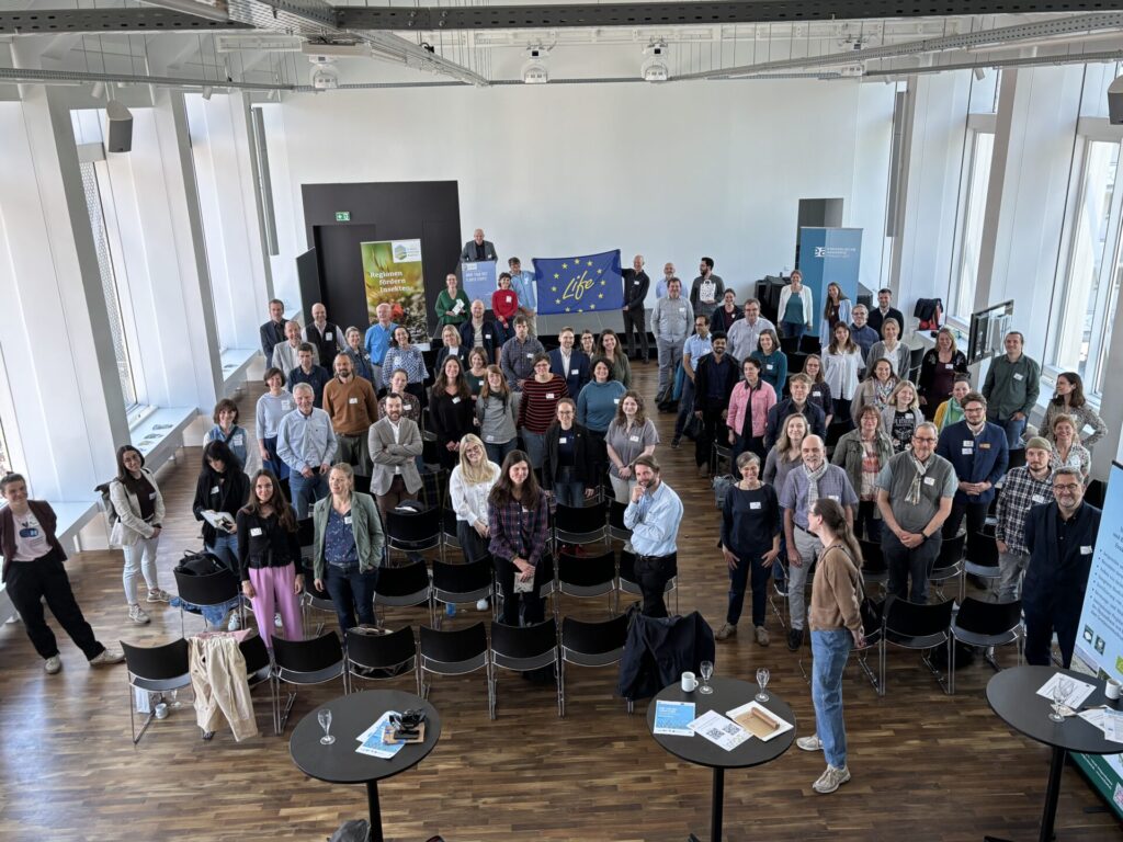 Gruppenfoto aus der Vogelperspektive. Im Hintergrund sieht man die Europaflagge. Mittig befindet sich ein Schriftzug mit "Life"