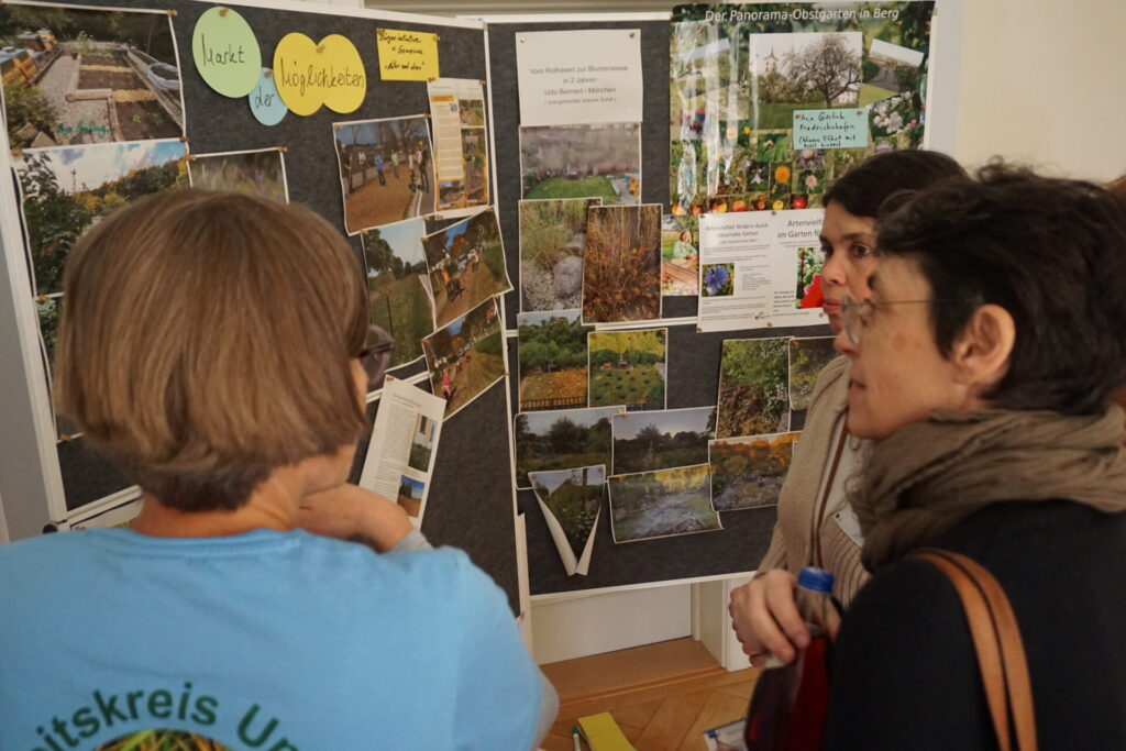 Drei Teilnehmer*innen stehen vor zwei großen Leinwänden, die den Markt der Möglichkeiten darstellen. Dort sind umgesetzte Projekte der Blühbotschafter*innen zu sehen.
