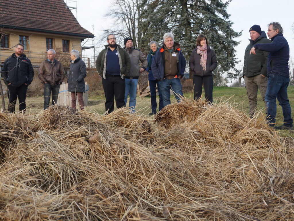 Eine Gruppe von Menschen steht hinter einer Kompostmiete, die im Vordergrund zu sehen ist.