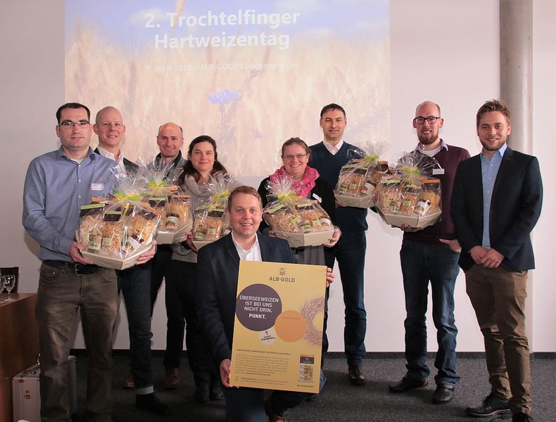 Eine Gruppe von 9 Personen steht zusammen und schaut in die Kamera. 7 Personen halten jeweils einen Geschenkkorb mit Nudelpackungen, eine Person kniet vor der Gruppe und hält ein Poster, auf dem der Schriftzug Alb-Gold zu erkennen ist.